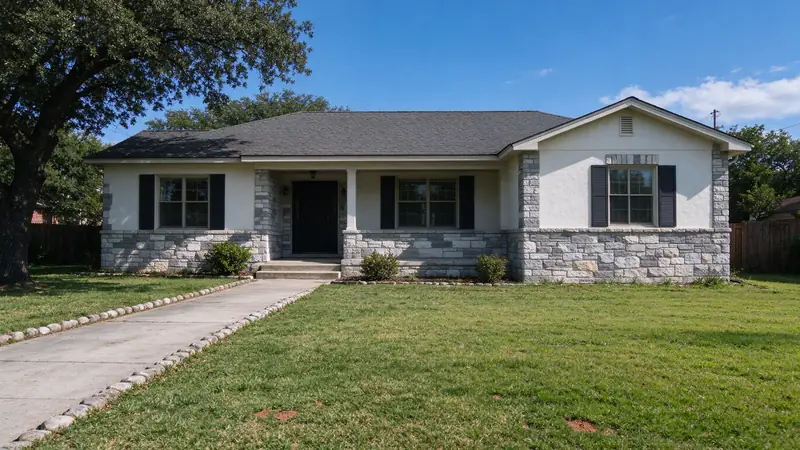 Older stone and stucco house with a narrow concrete driveway and a mature live oak